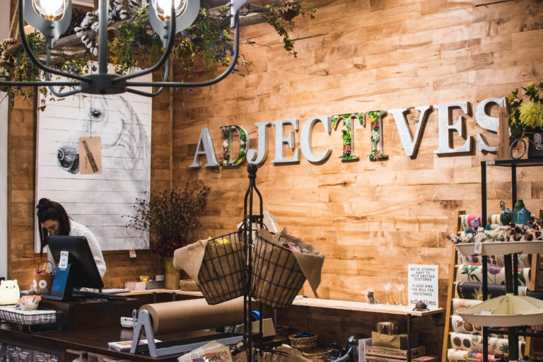 Adjectives spelled out in large metal letters on the wall behind the cashier area at Adjectives Market on Park Avenue.