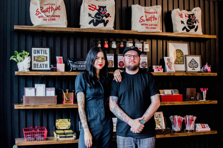 Clark Orr and Brittany Reagan pose in front of a wall of product in their store, Hellcats USA.