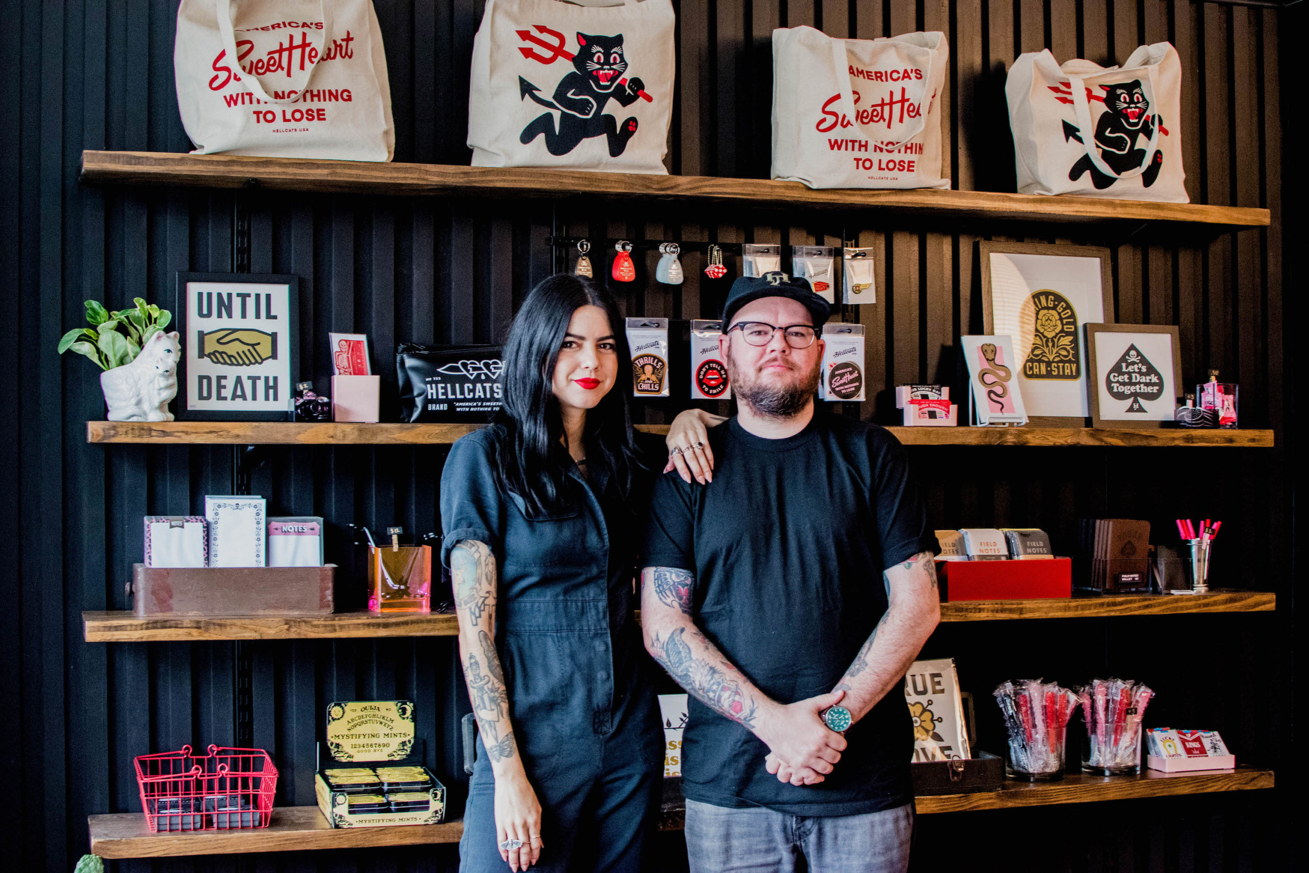Clark Orr and Brittany Reagan pose in front of a wall of product in their store, Hellcats USA.