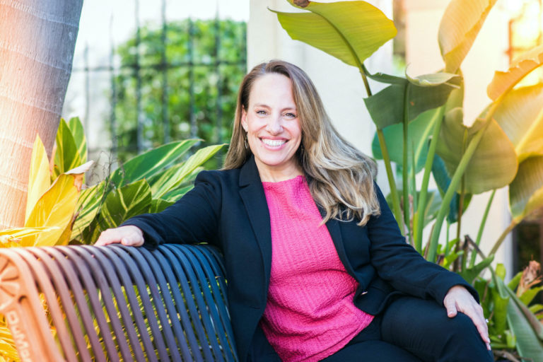 Colette Fehr sitting on a bench in front of green foliage.