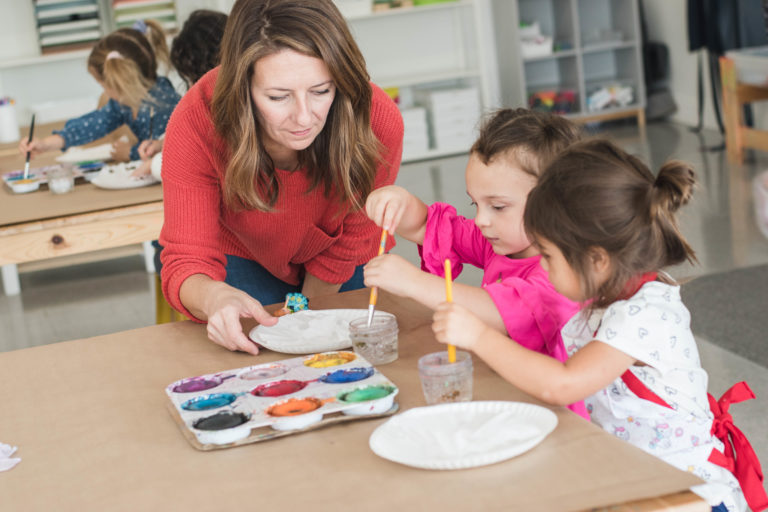 Woman shows young girls how to paint.