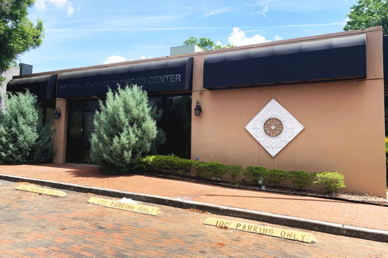 A tan building with a green bush outside of the parking lot under a blue sky.