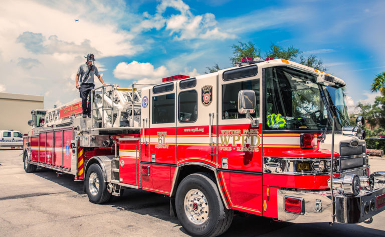 A red firetruck with a fireman on the back and a blue sky