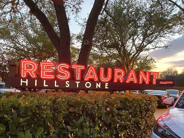 Red Hillstone sign lit up and hovering over a green bush