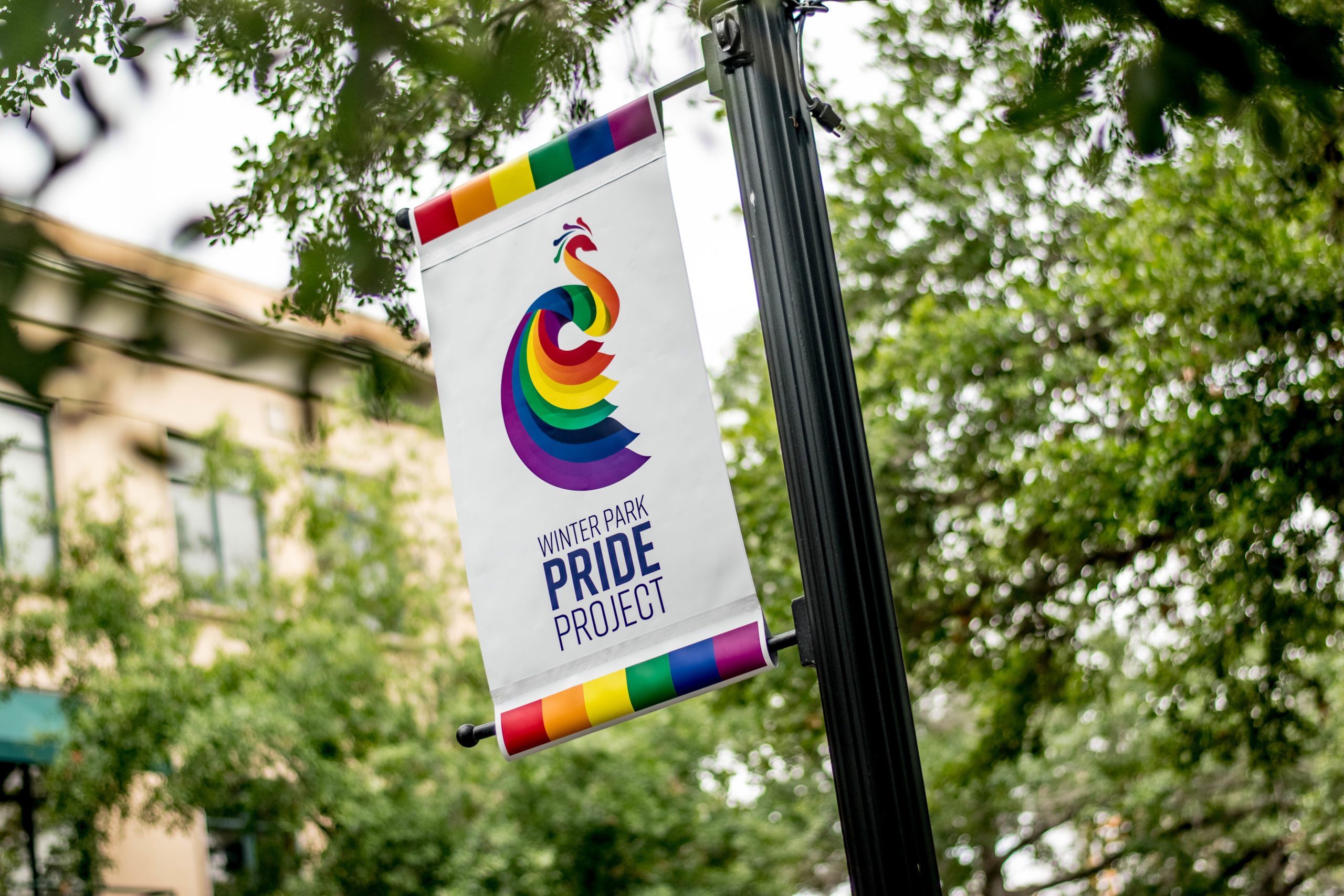 A flag pole shows a Winter Park Pride flag hanging with rainbows in front of green trees.