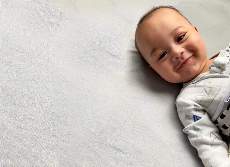 Grey background shows peach colored baby with a grey shirt smiling