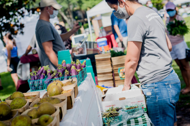Image shows woman in grey t-shirt with blue jeans and various fruits and vegetables on a white table.