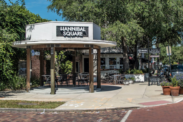 A white and brown, brick and wood building in Hannibal Square with green trees