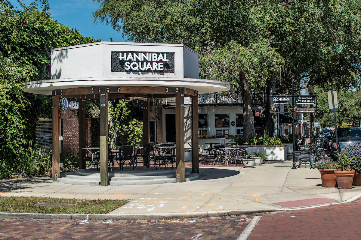 A white and brown, brick and wood building in Hannibal Square with green trees